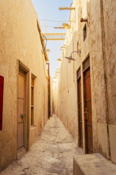 Doha Qatar Katara Cultural Village narrow traditional alley mud brick walls heritage architecture sun flare travel tourism Middle East Qatari culture exploration sunny