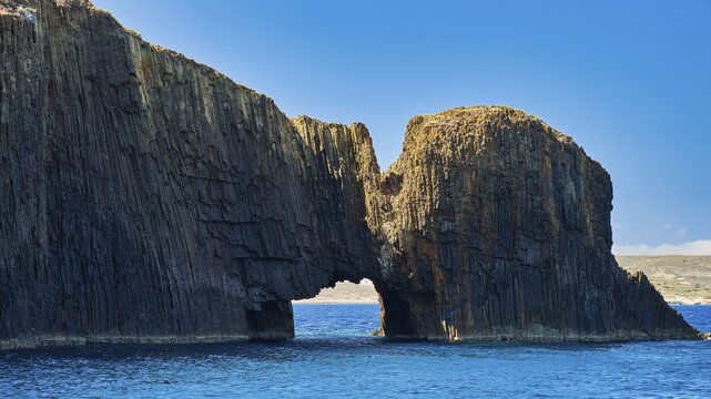 A large rock formation juts out of the blue sea, with a clear blue sky, Glaronisia, Glaronesia, Milos, islets, hexagonal basalt columns, north of Milos, destination by boat, Cyclades, Greek Islands, Greece