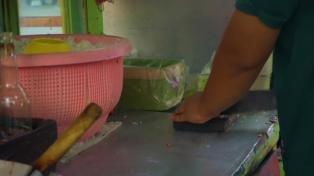 A local street food vendor chopping shallots with a knife on a wooden board at a traditional food stall, preparing ingredients for fried rice cooking.