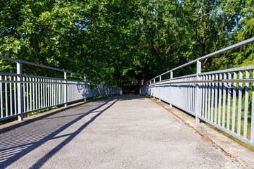 Fototapeta premium Concrete pedestrian bridge with metal railings leading through green trees