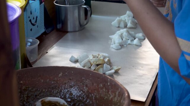 A local street food vendor cutting tofu and rice cake with a knife at a traditional stall, preparing a popular regional culinary dish.