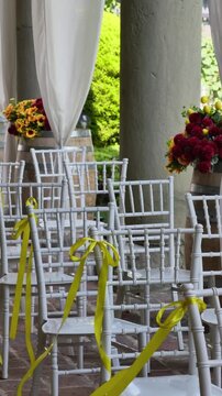 Elegant white chiavari chairs decorated with yellow ribbons for an outdoor wedding ceremony, featuring flower arrangements with sunflowers and red dahlias on wooden barrels