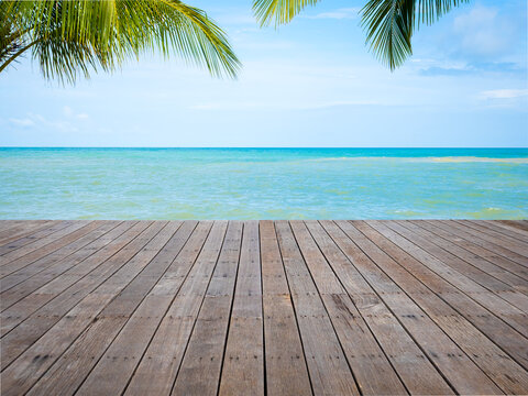 Wooden deck overlooking tropical beach with turquoise sea, palm leaves, blue sky, and copy space, perfect for summer vacation, travel, tourism, resort, product display, and beach background.