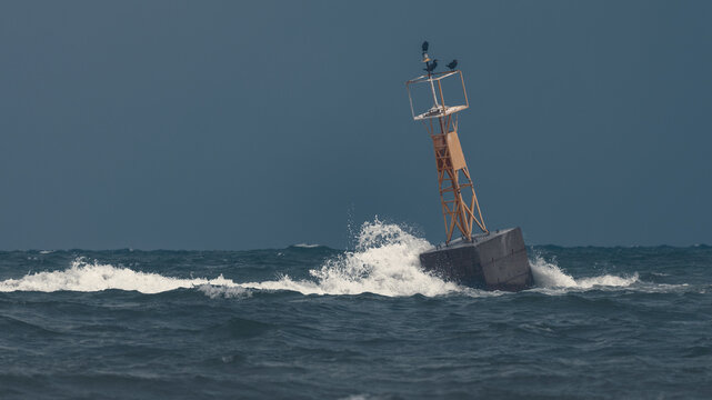 Large yellow sea buoy or navigation beacon crashing through rough waves and sea foam during a storm