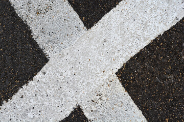 A close up top down view of thick weathered white painted lines crossing on a dark textured asphalt road surface. © nahhan