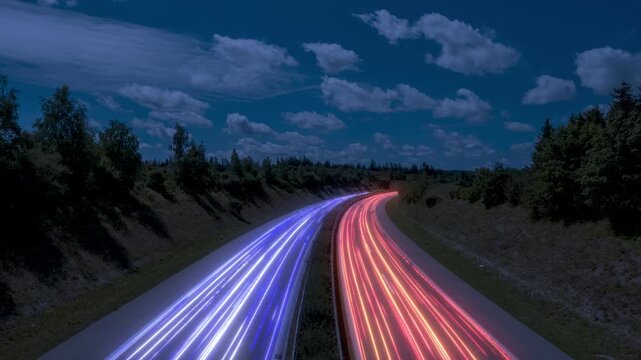 Abstract dynamic light streaks on a highway at night, showing white, blue, red and orange vehicle trail lights against a dark forest and cloudy blue sky, seamless loop, ideal for tech logistic themes
