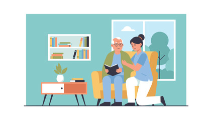 Fototapeta premium Caring young female nurse supports an elderly man who is sitting in an armchair reading a book at home.
