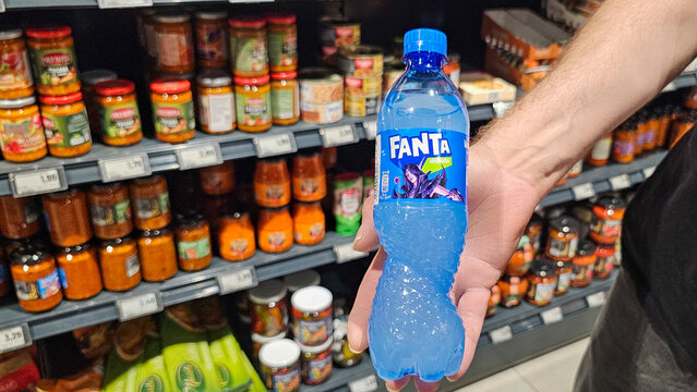 Hand holding fanta blue beverage in supermarket aisle