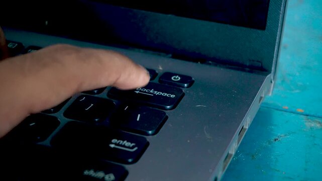 Close up of a person pressing the backspace key repeatedly on a computer laptop keyboard, highlighting digital office work, text editing mistakes, and technology use.