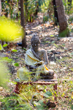A stone hermit statue wearing a yellow cloth sitting in meditation posture in a forest