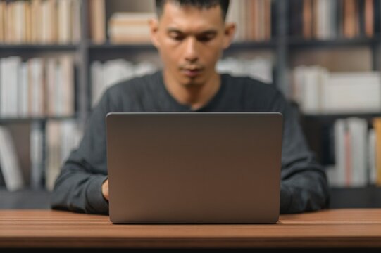 Young Man Using Laptop at Desk in Library with Bookshelves Background