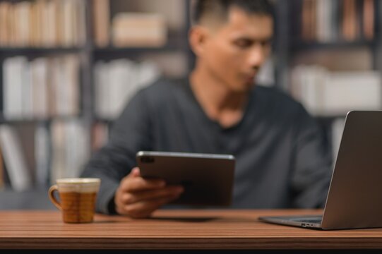 Modern man using tablet and laptop at desk in cozy library setting