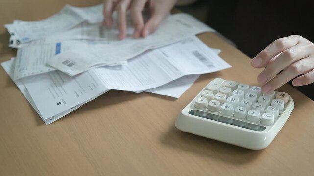 Person calculating monthly household bills with receipts, invoices, credit cards and a calculator for debt management and family expense planning.