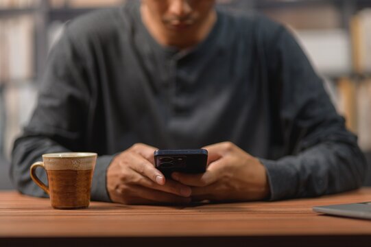 Man Using Smartphone with Coffee Mug on Wooden Table in Indoor Cafe Setting