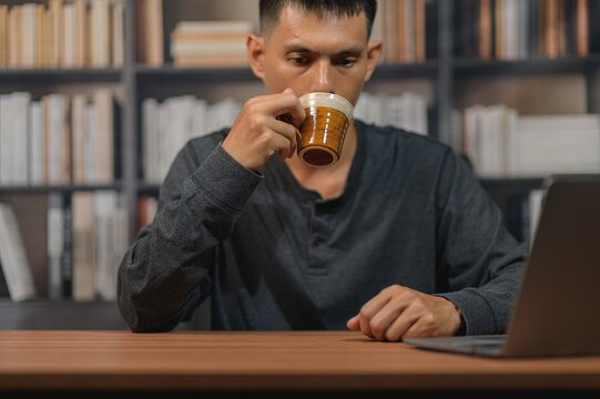 Young man enjoying coffee while working on laptop in a modern library setting