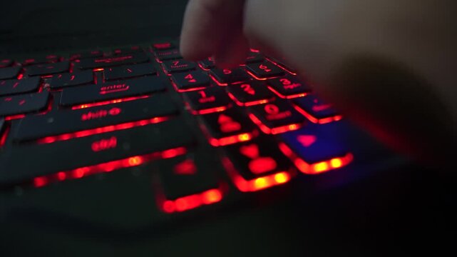 Close up of a person using a numeric keypad on a laptop computer with glowing red backlit keys, capturing financial calculations, accounting work, and data entry tasks.