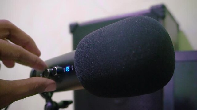 A person turning on a microphone for a voice over recording, capturing audio production, podcast setup, and professional sound broadcasting in a studio.