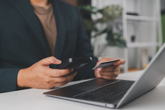 Online payment and e-commerce shopping concept. Man holding credit card and using smartphone at desk with laptop.