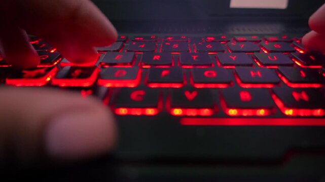 Smooth sideways slide movement capturing a macro close up of a gamer playing on a laptop computer with glowing red backlit keys, highlighting esports and gaming technology.