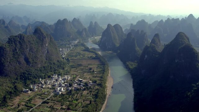 Aerial view of karst mountains flanking a winding river, with a rural village and farmland in the valley.