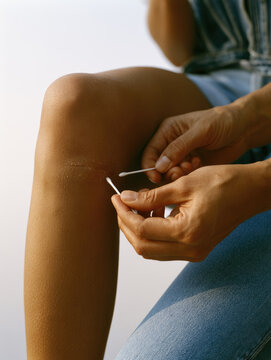 Knee scrape wound care with cotton swab, natural hand cleaning skin in bright soft light, simple close up with blank background and calm relief