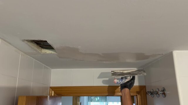 Repairman plastering a water damaged ceiling with a putty knife