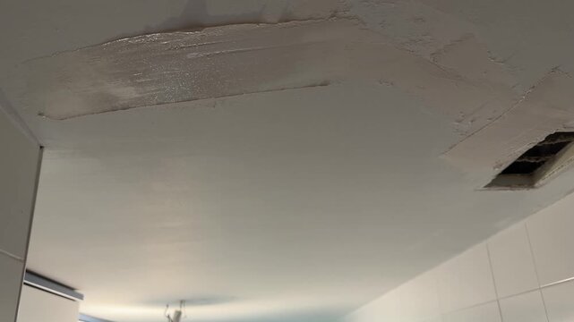 Handyman applying plaster to a damaged ceiling with a trowel