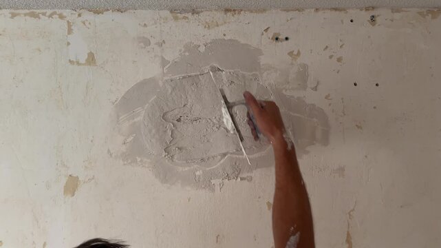 Plasterer applying putty to repair a damaged wall