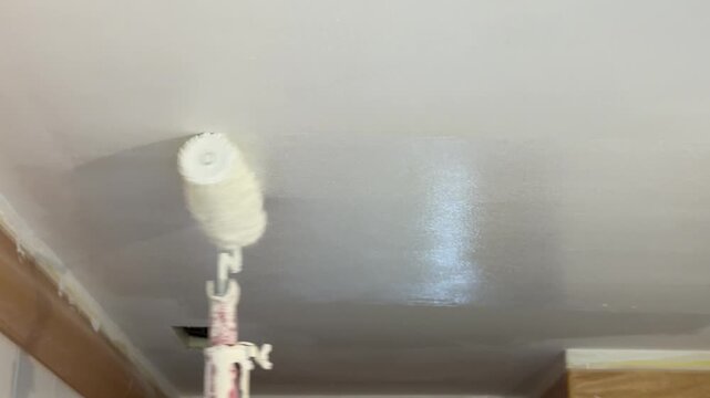House painter painting bathroom ceiling with roller