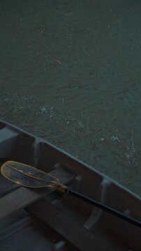 Small boat with paddle during rainfall on canal water, Raindrops splashing around rowing boat with wooden seat and paddle on water surface, 4k vertical video