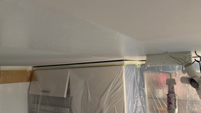 Worker painting a white ceiling with a paint roller