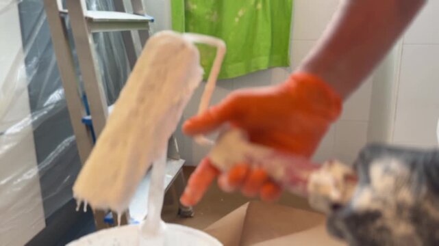 Professional painter dipping a roller into a white paint bucket