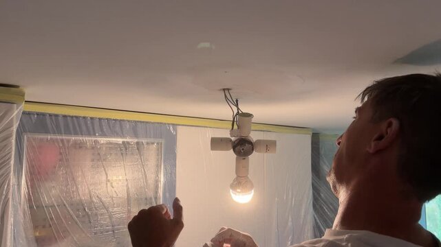 Electrician handyman removing a ceiling lamp for renovation