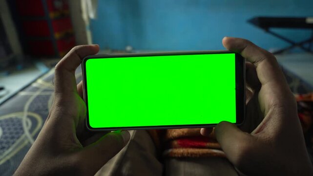 Static horizontal smartphone display with a green screen held by a person in a room, capturing clean mobile device mockups, chroma key technology, and digital media concepts.