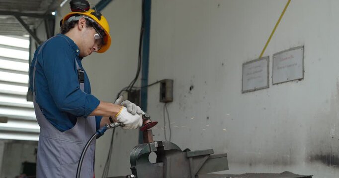 Factory worker using handheld grinder to cut metal workpiece in bench vise at workshop