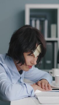A woman in an office sits at her desk with her head down. She struggles to stay awake while working on her computer and tries to refocus her attention after a moment of rest.