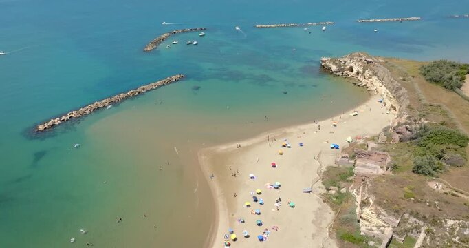 Aerial view of Grotte di Nerone Beach in Anzio, Italy, showing the sandy cove with beach umbrellas, adjacent to ancient Roman ruins and sea caves, and protected by breakwaters in the Tyrrhenian Sea.