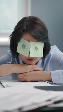 A woman at her desk uses stickers on her eyes while resting. The setting is a typical office environment during the day as she takes a short break.