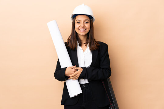 Young architect woman holding blueprints over isolated background laughing