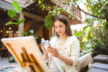 Gen Z Influencer content creator woman using smartphone with creativity leisure painting brush on canvas at workshop cafe © dodotone
