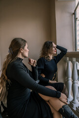 Obraz premium Women Balcony Winter Fashion: Two women in black dresses sit on a balcony, possibly during winter, showcasing autumn/winter fashion.