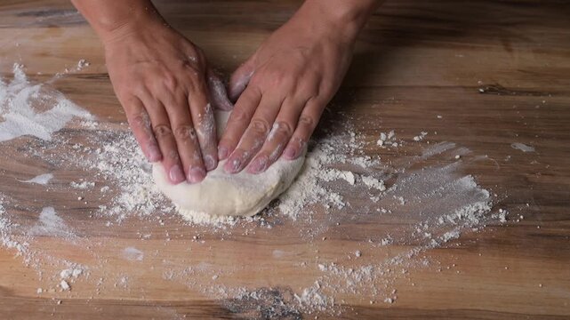 Close up baker hands kneading fresh pizza dough on wooden board with flour, traditional Italian cooking in pizzeria kitchen