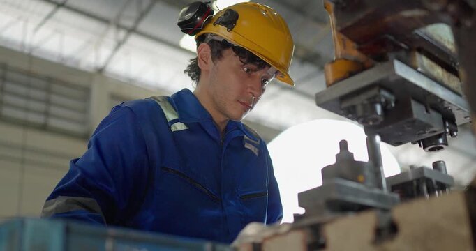 Focused factory worker in blue coverall operating and adjusting metal press machine in factory