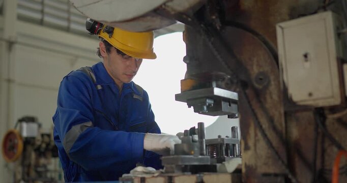 Focused factory worker in blue coverall operating and adjusting metal press machine in factory