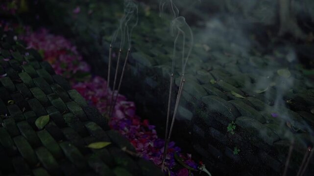 Burning incense sticks with gentle smoke and flower petals on ancient stone in 4k video.