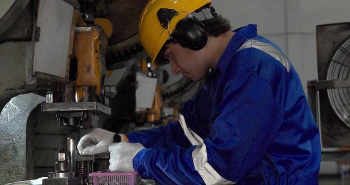 Focused factory worker in blue coverall operating and adjusting metal press machine in factory