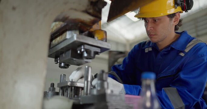 Focused factory worker in blue coverall operating and adjusting metal press machine in factory