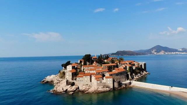 Aerial drone view of Sveti Stefan featuring the iconic fortified island surrounded by the crystal clear Adriatic Sea on the beautiful coast of Montenegro.