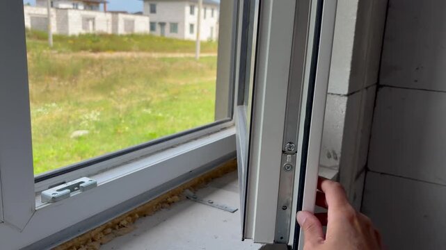 a hand opening and closing a white PVC window in an unfinished house under construction