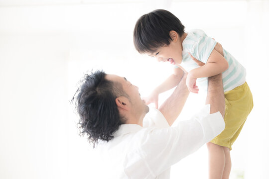 逆光の中子どもを高い高いをして、抱っこして遊ぶ父親 親子のふれあい・育児や子育て、成長の明るいイメージ